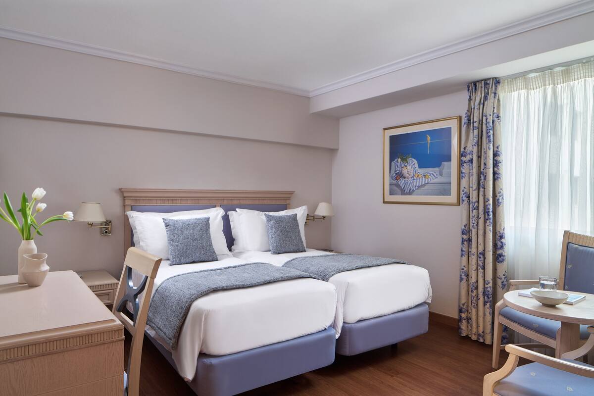 Una cama doble con cabecera, una mesita de noche con lámpara, un jarrón con flores y un cuadro en la pared.