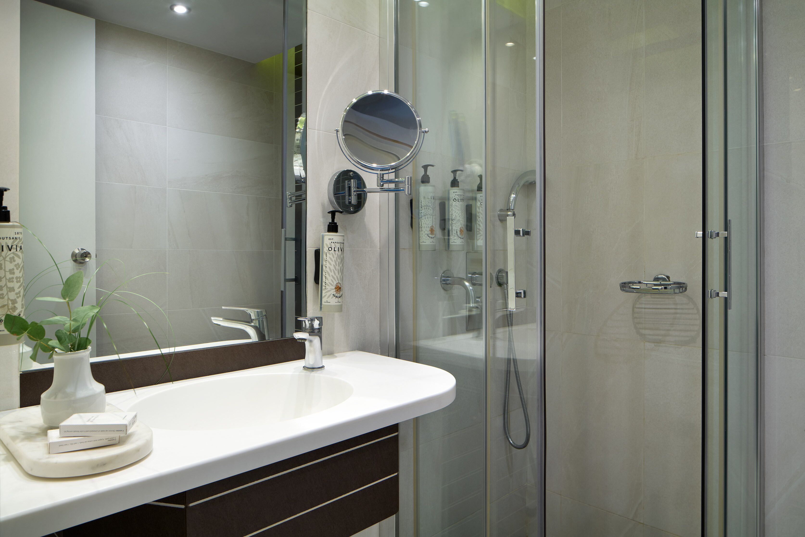A modern bathroom with a glass-enclosed shower, a white sink, and a mirror.
