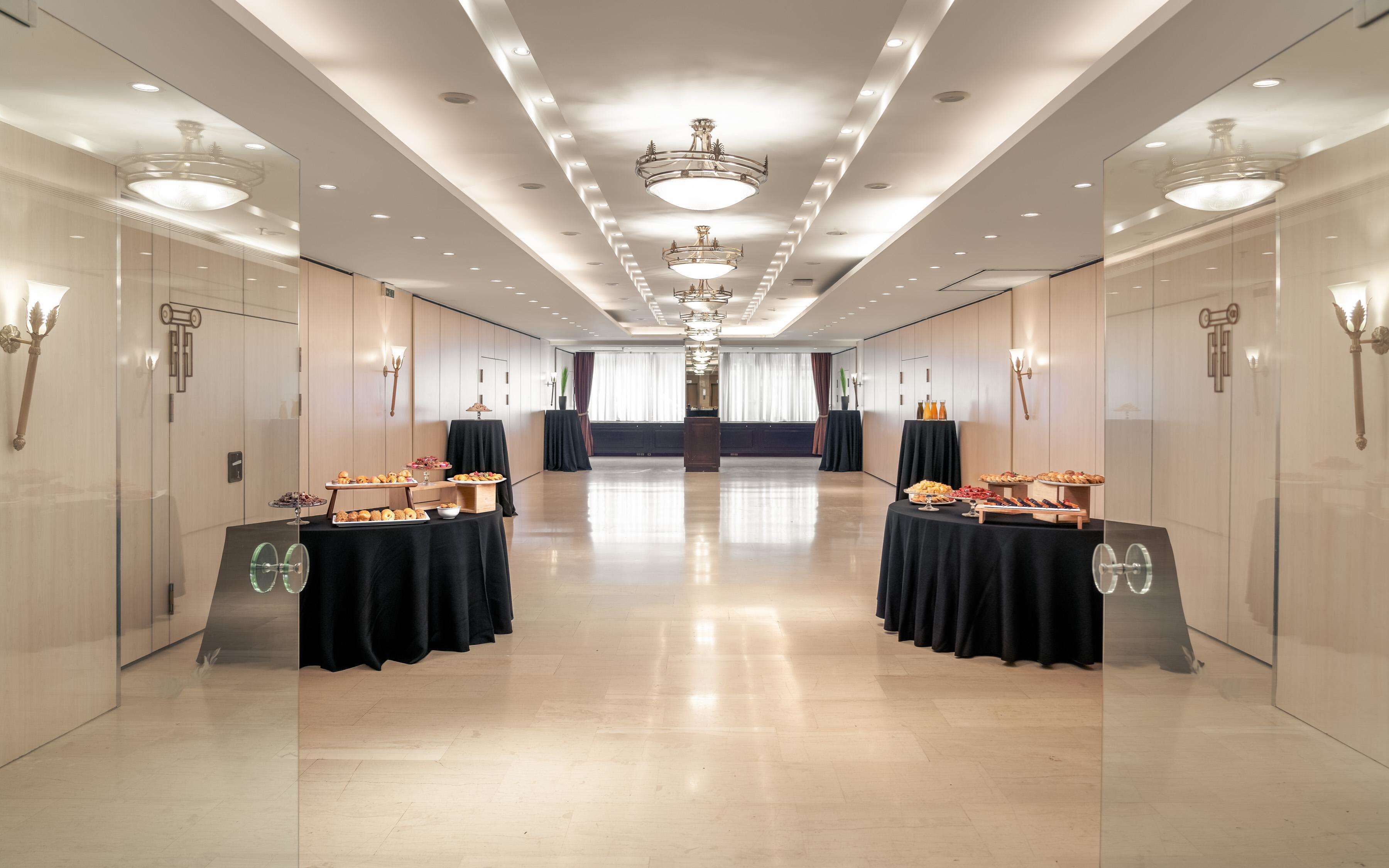 A spacious, well-lit corridor with tables set up for a buffet, featuring various food items.
