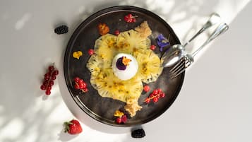 Un plato de postre con una esfera blanca en el centro, rodeada de fruta cortada y bayas, sobre un plato oscuro.
