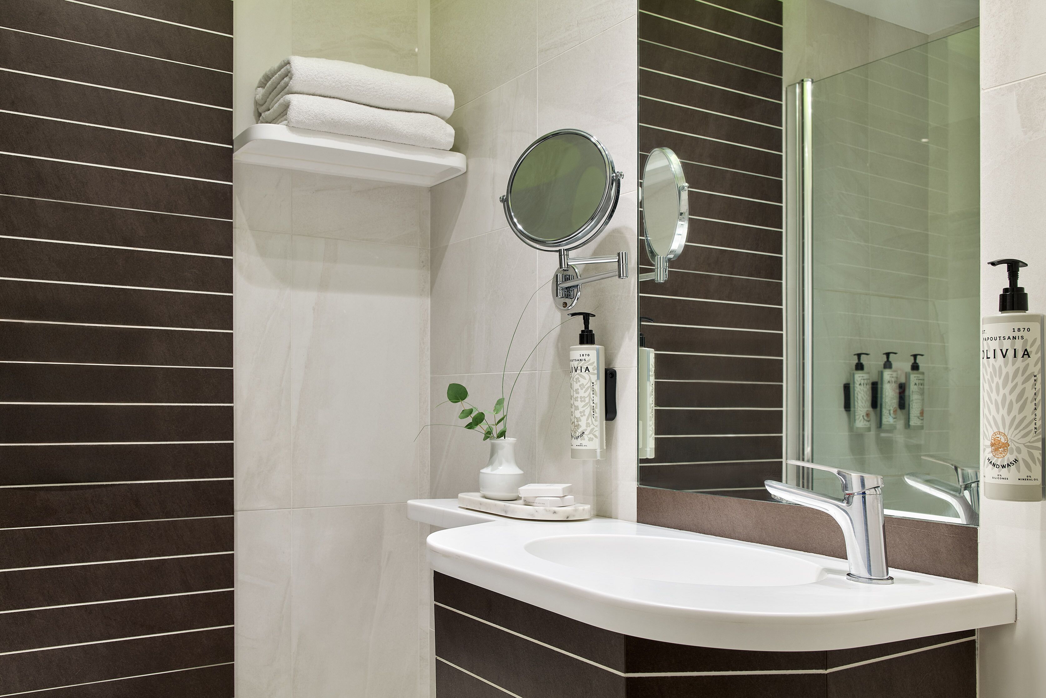 Een moderne badkamer met een witte wasbak, een ronde spiegel en een douchecabine van glas.