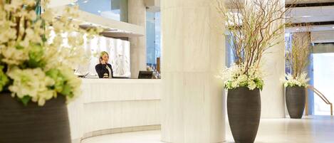 A modern reception area with a curved counter, large columns, and potted plants.