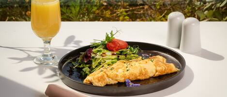 A meal with a glass of orange juice, a plate of food, and a napkin on a table with a view of greenery.