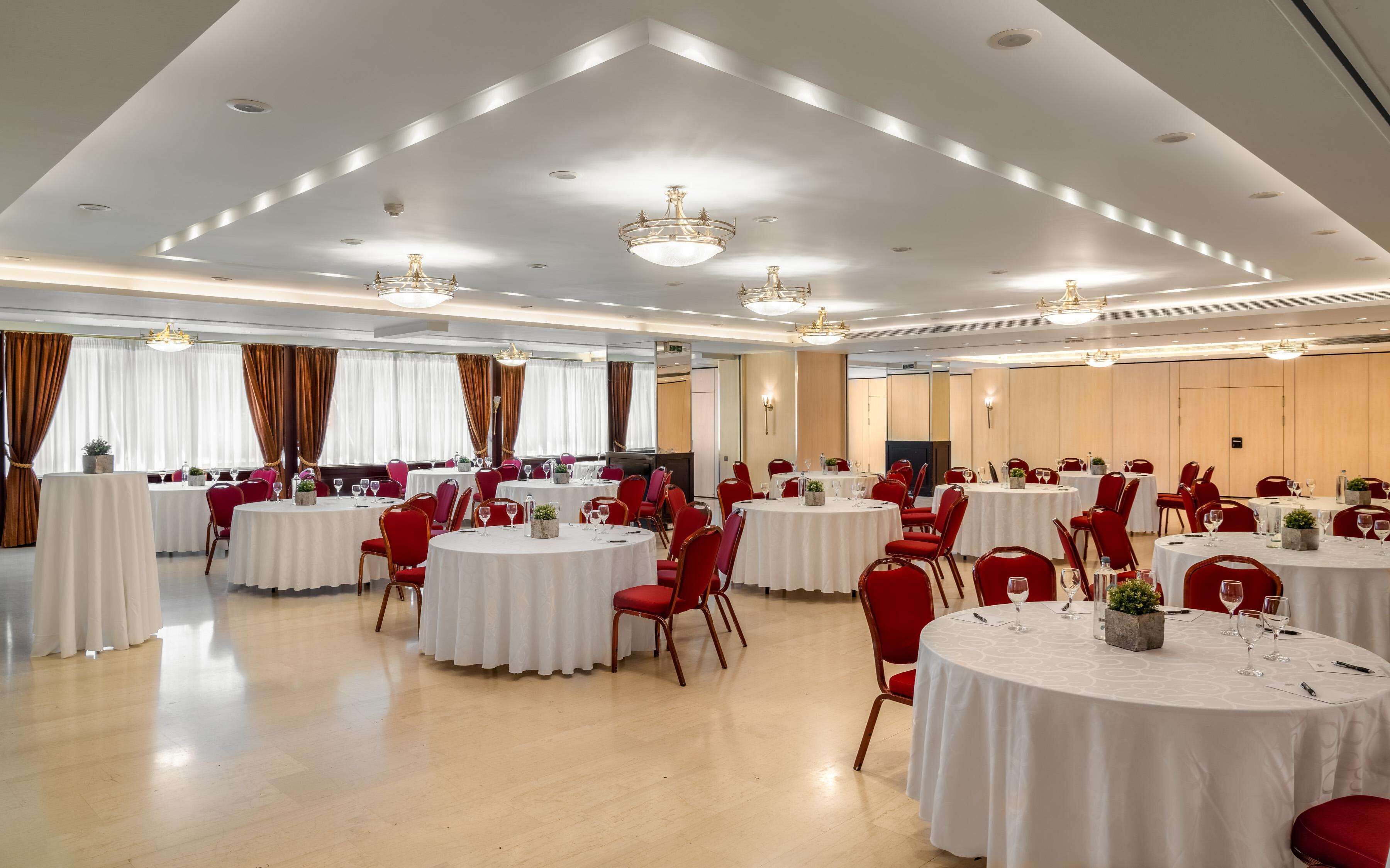 Une salle de banquet avec des tables rondes, des chaises rouges et des lustres.