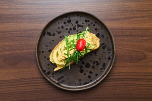 Un plato con un sándwich sobre una losa de cerámica oscura con motas.