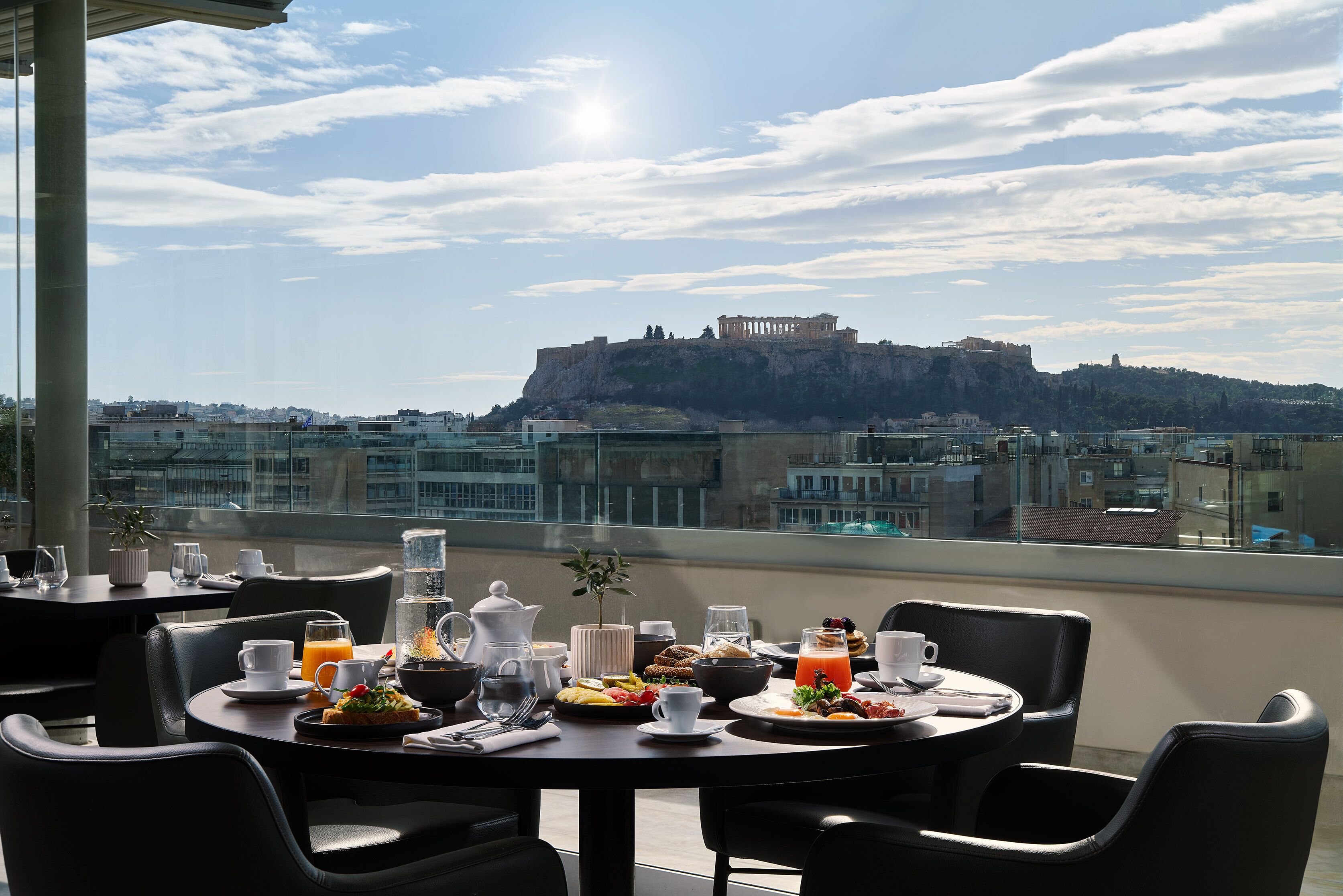 A rooftop dining area with tables set for breakfast, overlooking a historic castle on a hill.