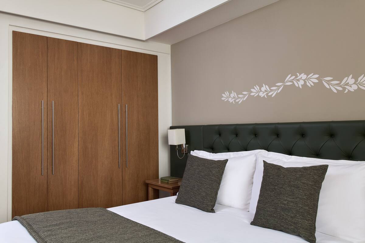 Habitación de hotel con un armario grande, una cama con almohadas blancas y oscuras, y una pared con diseño floral.