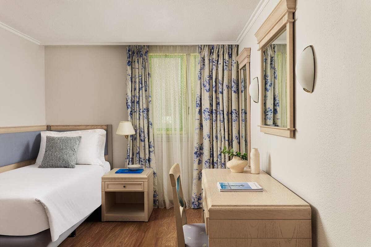 Una habitación de hotel con cama, mesita de noche, silla, escritorio y un espejo.