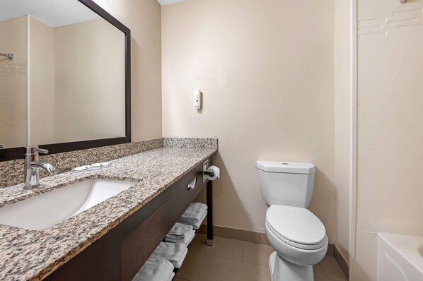 A bathroom with a granite countertop sink, a mirror, a toilet, and a towel rack.