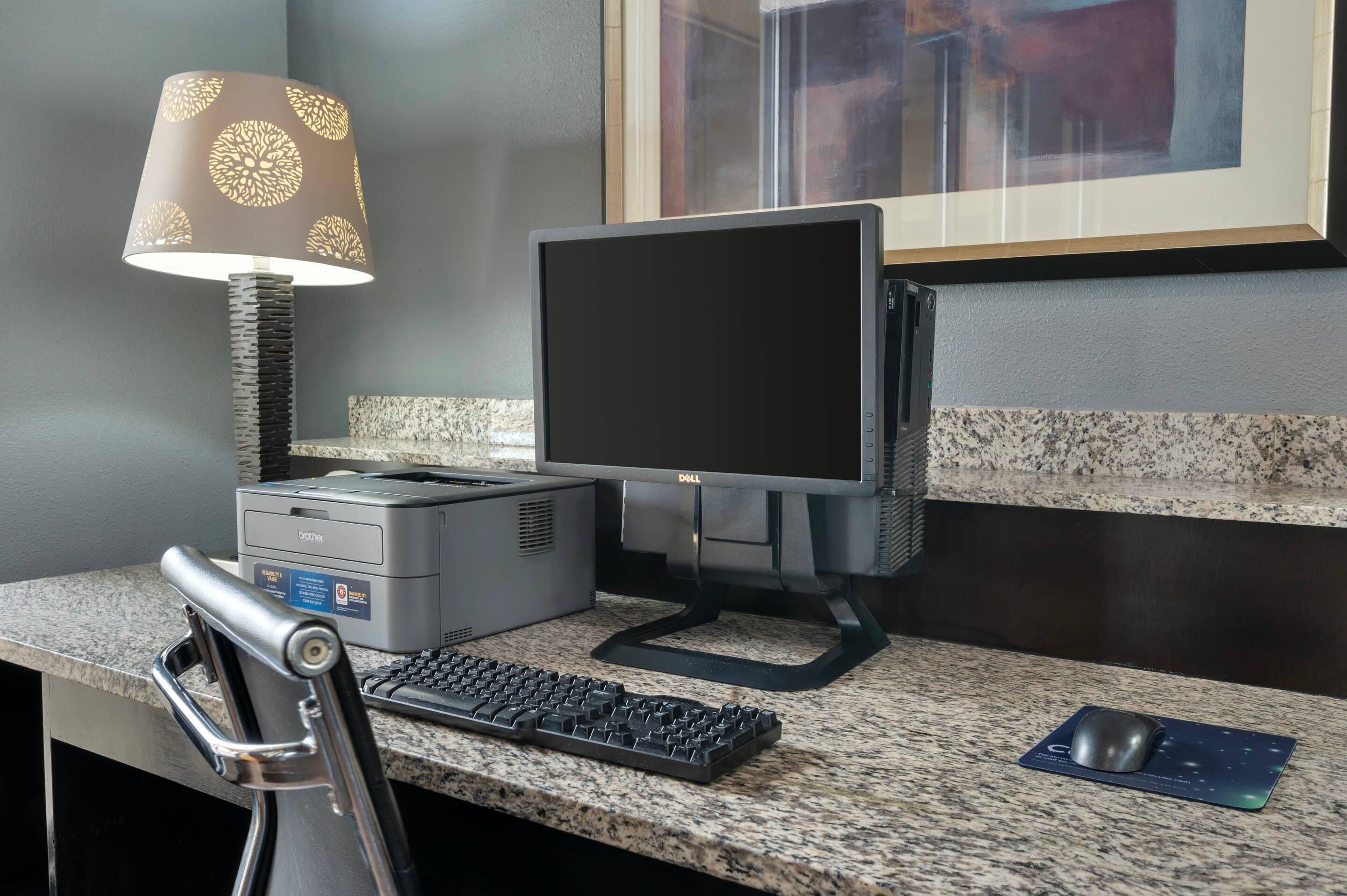 Un bureau avec un ordinateur, un clavier, une souris, une imprimante et une lampe.