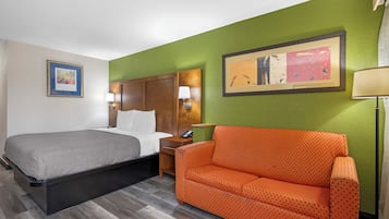 Een hotelkamer met een bed, nachtkastje, lamp, bank en twee ingelijste foto's aan de muur.