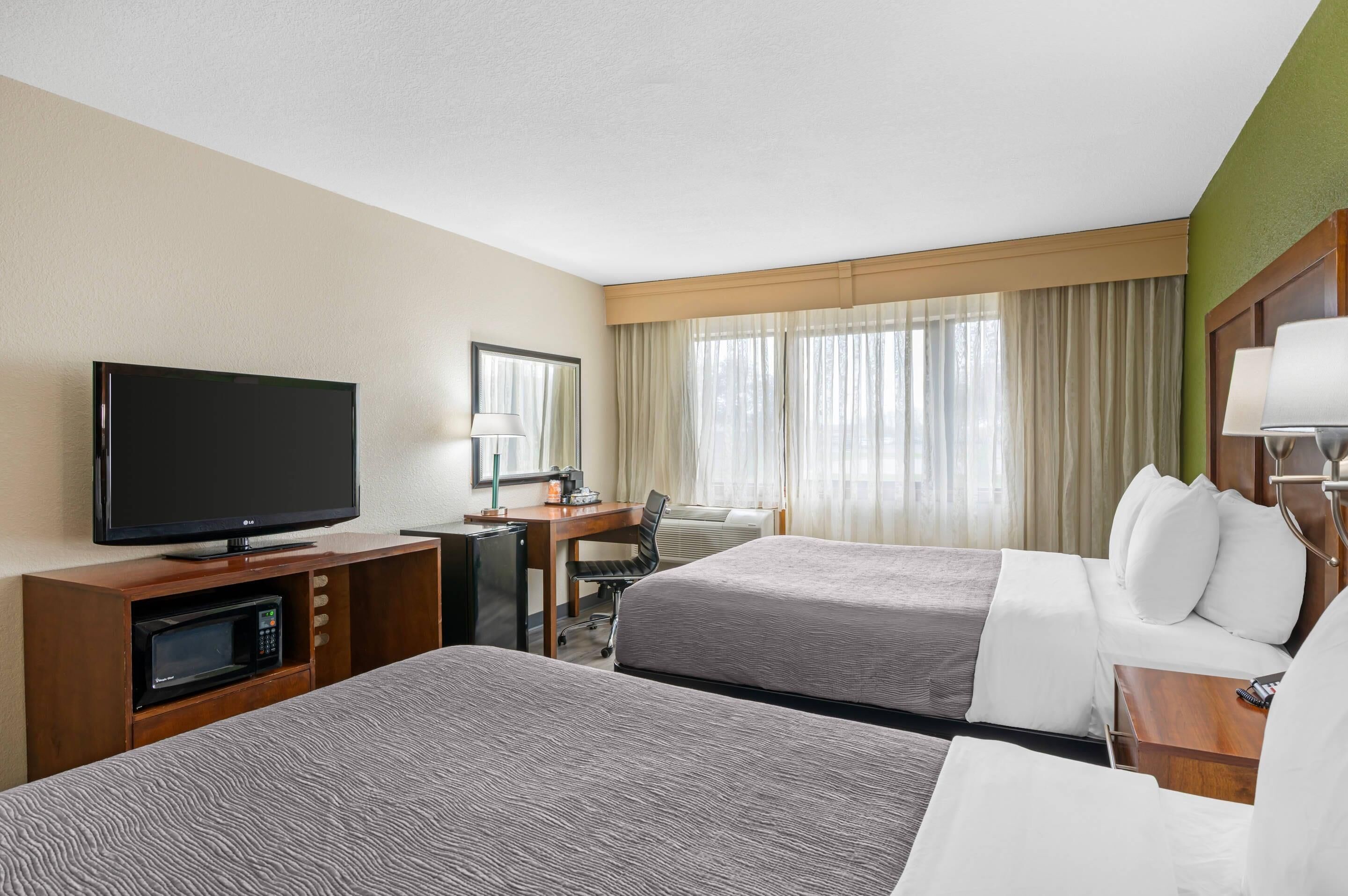 A hotel room with two beds, a TV, a desk with a chair, and a window with curtains.