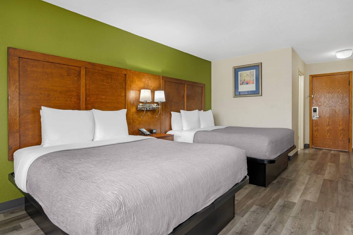A hotel room with two beds, a wooden headboard, bedside lamps, a framed picture on the wall, and a door.