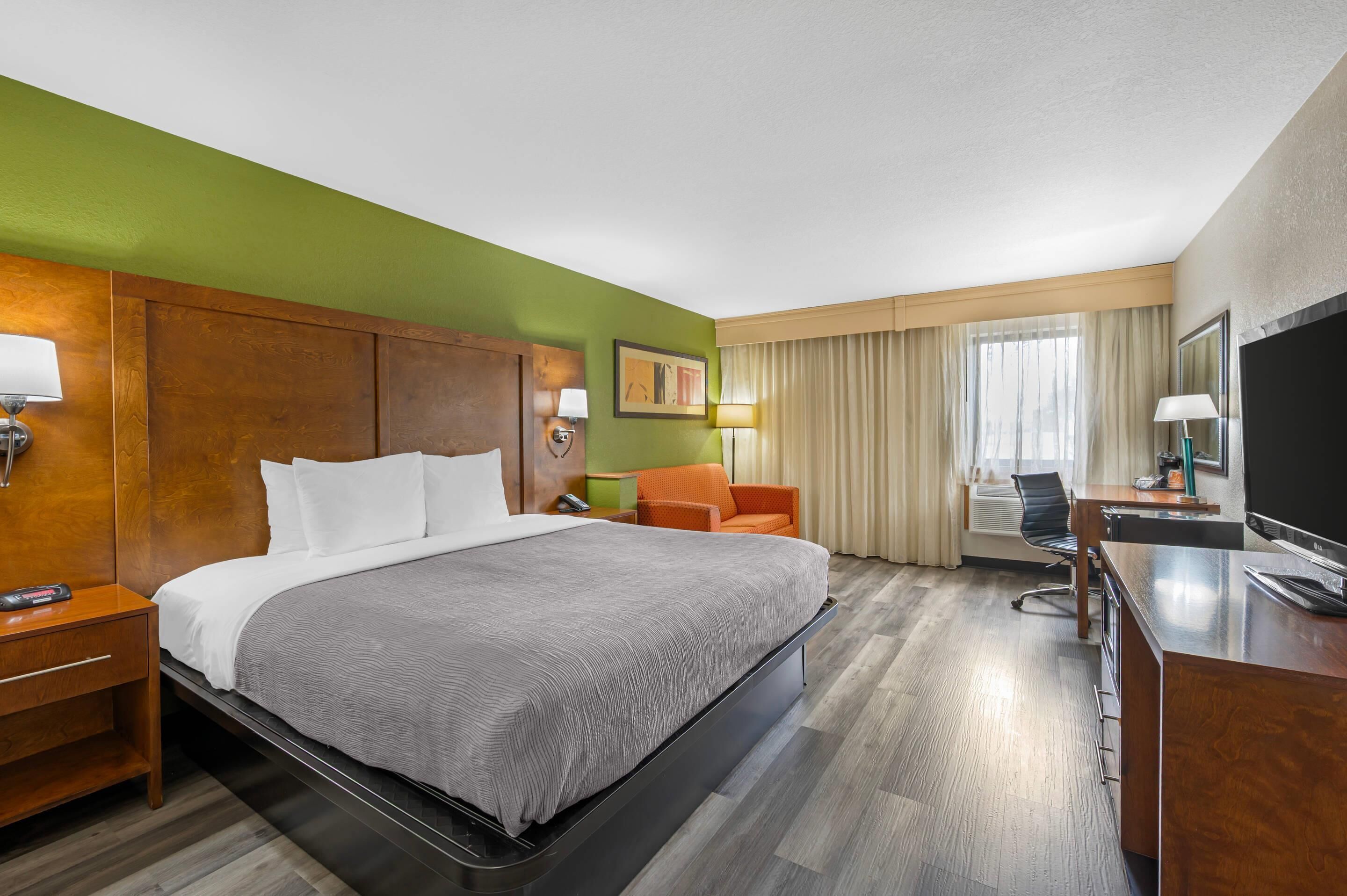 A hotel room with a bed, a desk, a chair, a TV, and a window with curtains.