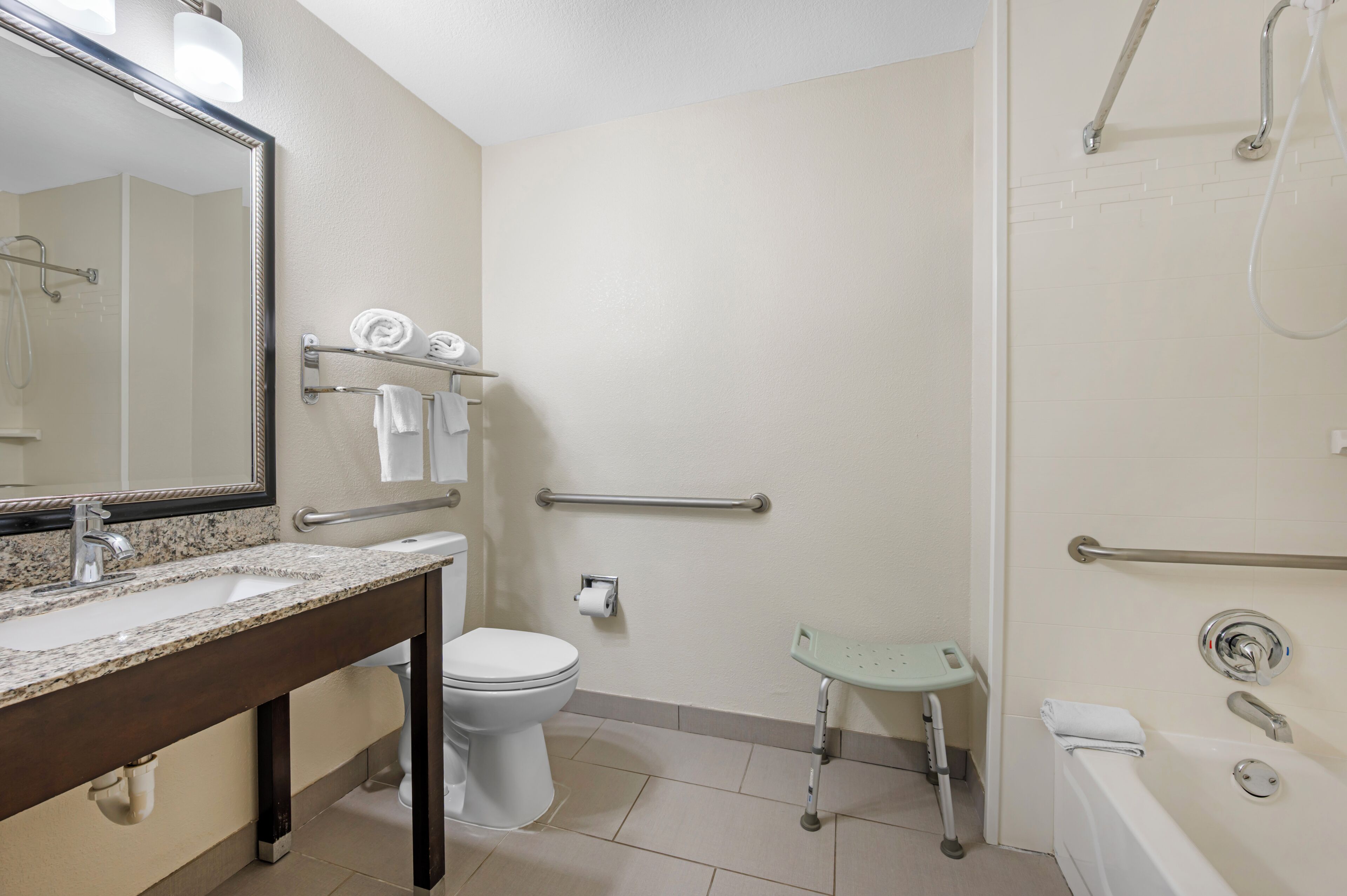 A bathroom with a sink, toilet, and shower area, including grab bars and a wheelchair-accessible bench.