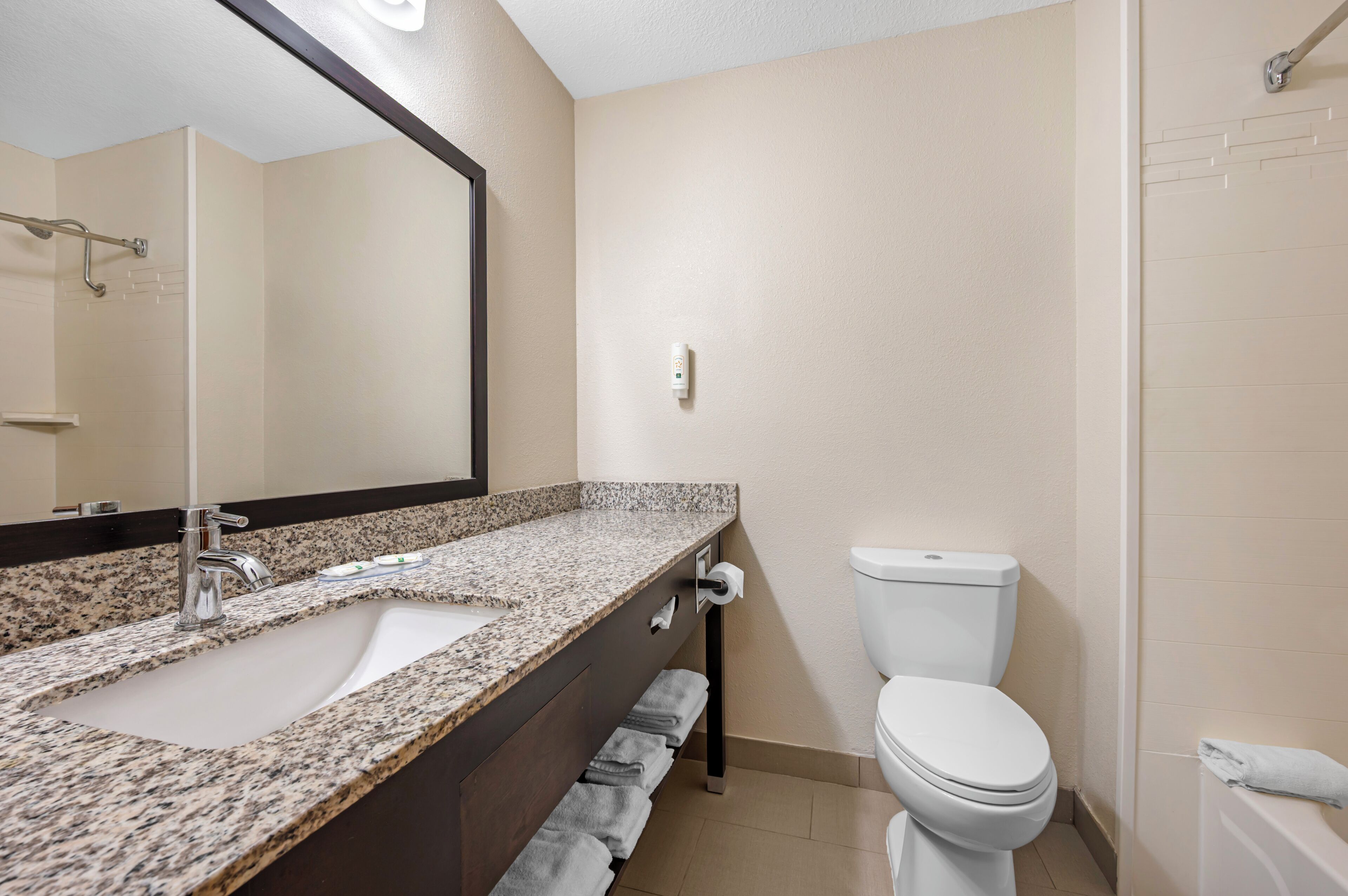 A bathroom with a granite countertop sink, a toilet, a towel rack, and a shower area.