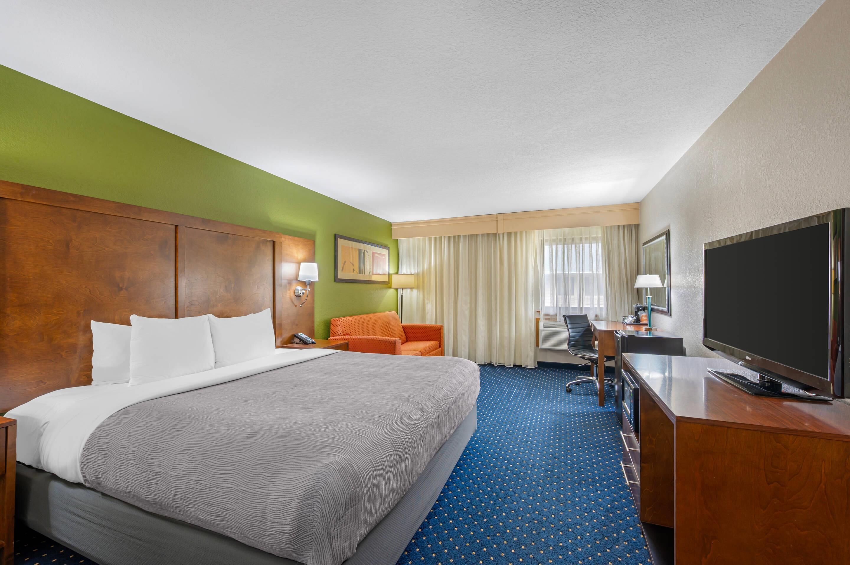 A hotel room with a large bed, a desk, a television, and a chair.