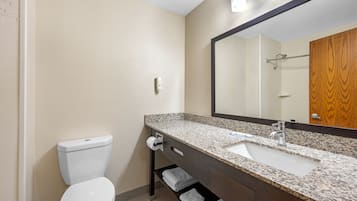 Un baño con inodoro, lavamanos, espejo, toallero y un panel de madera en la pared.