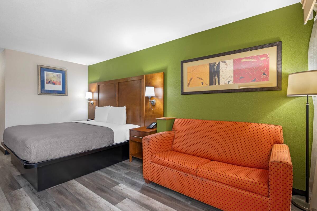 A hotel room with a bed, a nightstand, an orange sofa, and two wall-mounted lamps.