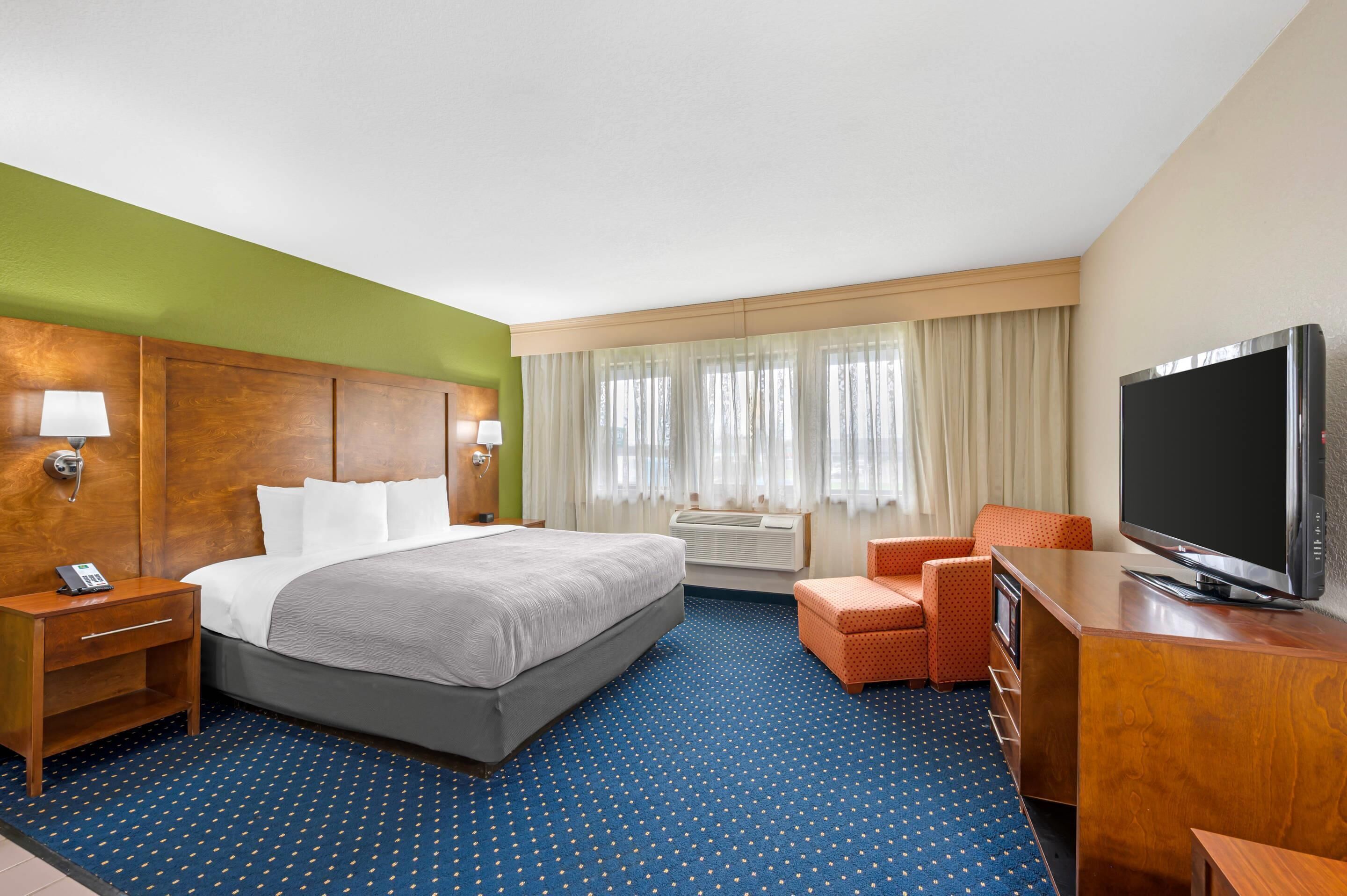 A hotel room with a bed, a TV, a desk, a chair, a lamp, and a window with curtains.