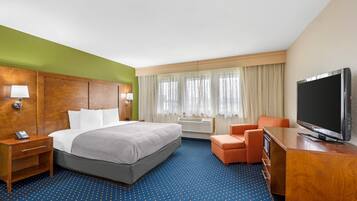 A hotel room with a bed, a TV, a desk, a chair, a lamp, and a window with curtains.