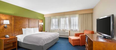 A hotel room with a bed, a TV, a desk, a chair, a lamp, and a window with curtains.