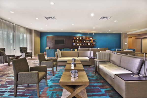 A hotel lobby with seating arrangements, a coffee table, and a bookshelf.
