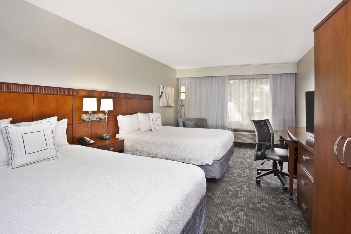 A hotel room with two beds, a desk, a chair, a TV, and a wardrobe.