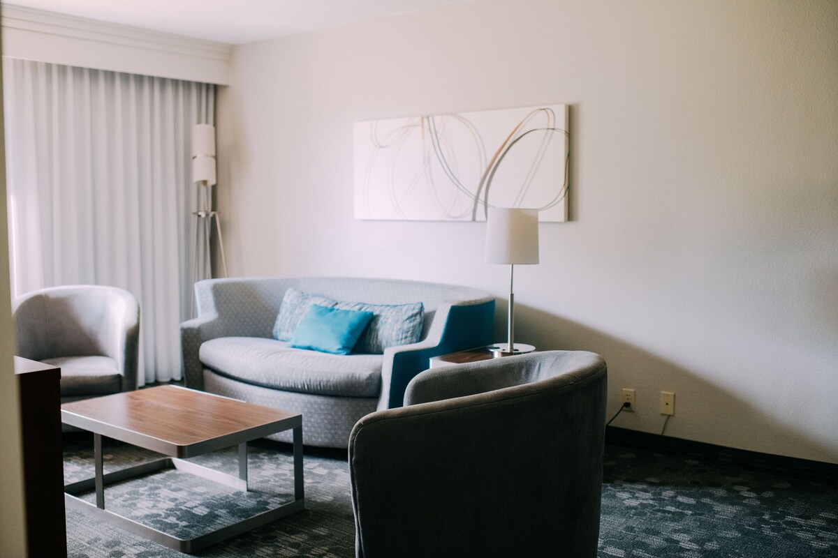 A modern hotel room with a grey sofa, a wooden coffee table, and a blue accent chair.