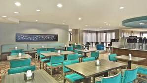 Un vestíbulo de hotel con varias zonas de estar, incluyendo una recepción, un bar y numerosas mesas y sillas.