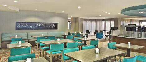 A hotel lobby with multiple seating areas, including a reception desk, a bar, and several tables and chairs.