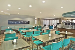Un vestíbulo de hotel con varias zonas de estar, incluyendo una recepción, un bar y numerosas mesas y sillas.