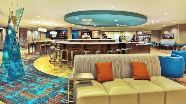 Un lobby moderno de hotel con un bar central, zonas de estar y una alfombra estampada.