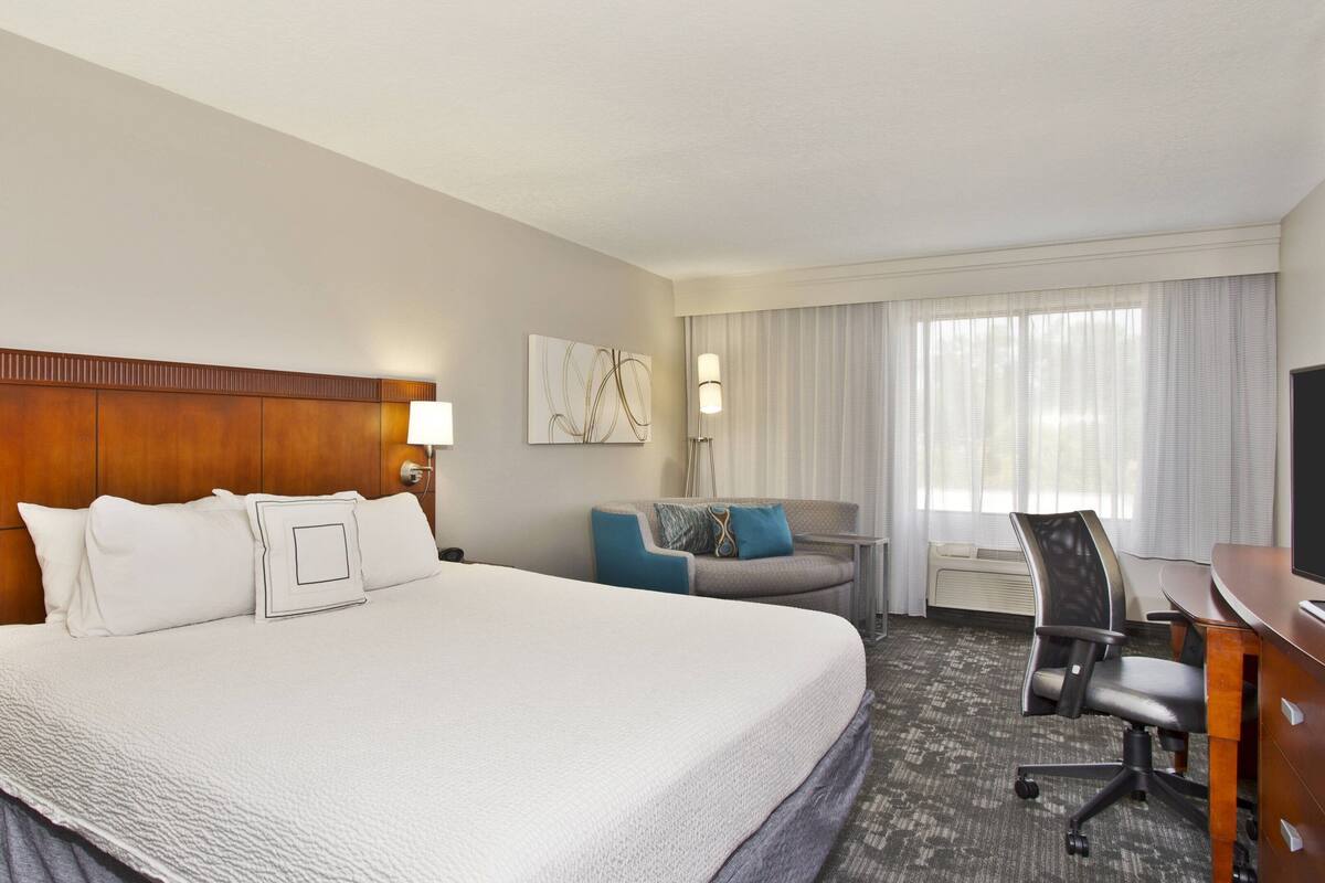 A hotel room with a large bed, a desk, a chair, and a window with curtains.