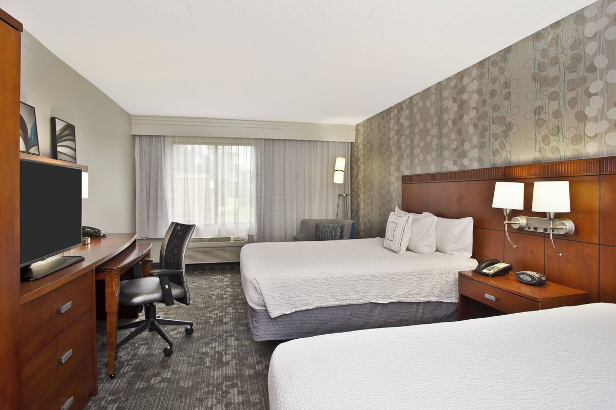 Ein Hotelzimmer mit zwei Betten, einem Schreibtisch, einem Computer, einem Fernseher und einem Telefon.