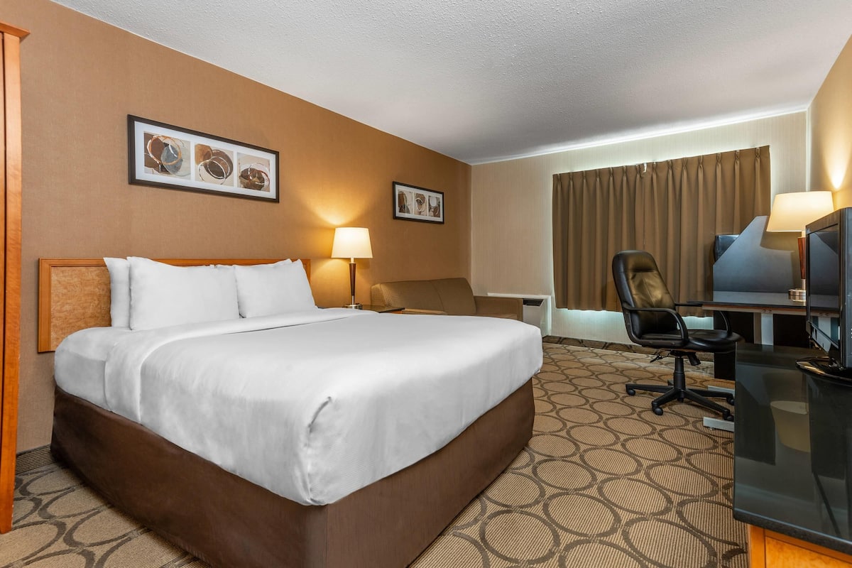 A hotel room with a large bed, a desk with a chair, a television, and two wall-mounted lamps.