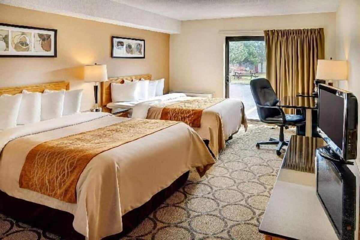 A hotel room with two beds, a desk with a computer, a chair, and a TV.