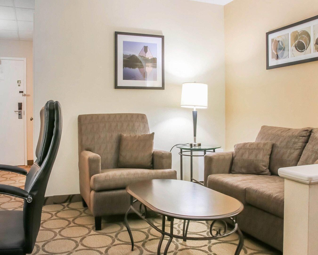 Habitación de hotel con sofá, sillón, mesita, lámpara y cuadros en la pared.