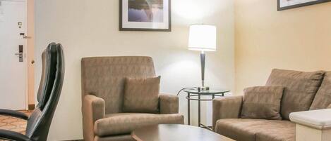 Habitación de hotel con sofá, sillón, mesita, lámpara y cuadros en la pared.