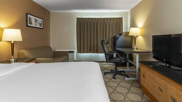 Une chambre d’hôtel avec un grand lit, un bureau avec un ordinateur, une télévision, deux lampes et une fenêtre avec des rideaux.