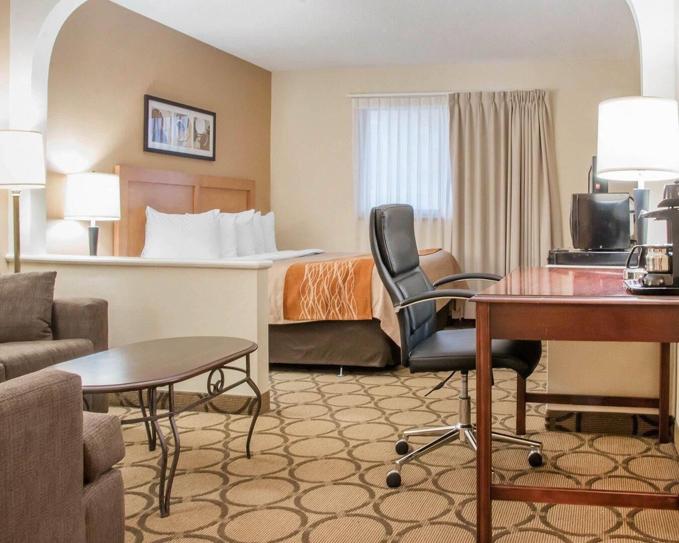 Een hotelkamer met een bed, een bureau, een stoel, een koffiezetapparaat en een lamp.
