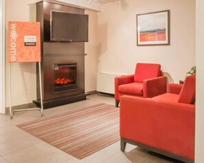 Una sala de estar moderna con chimenea, un televisor de pantalla plana, un sillón rojo y un letrero de bienvenida.