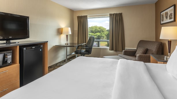 Una habitación de hotel con cama, escritorio, silla, televisor y refrigerador.