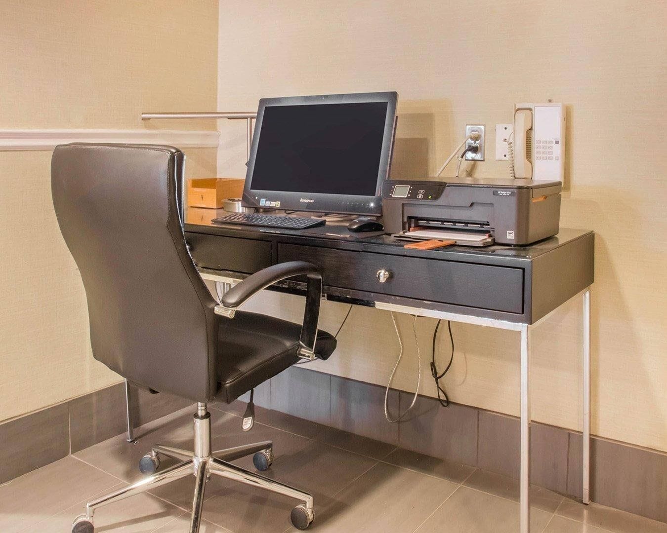 Un espacio de trabajo en un hotel con escritorio, computadora, impresora y silla.