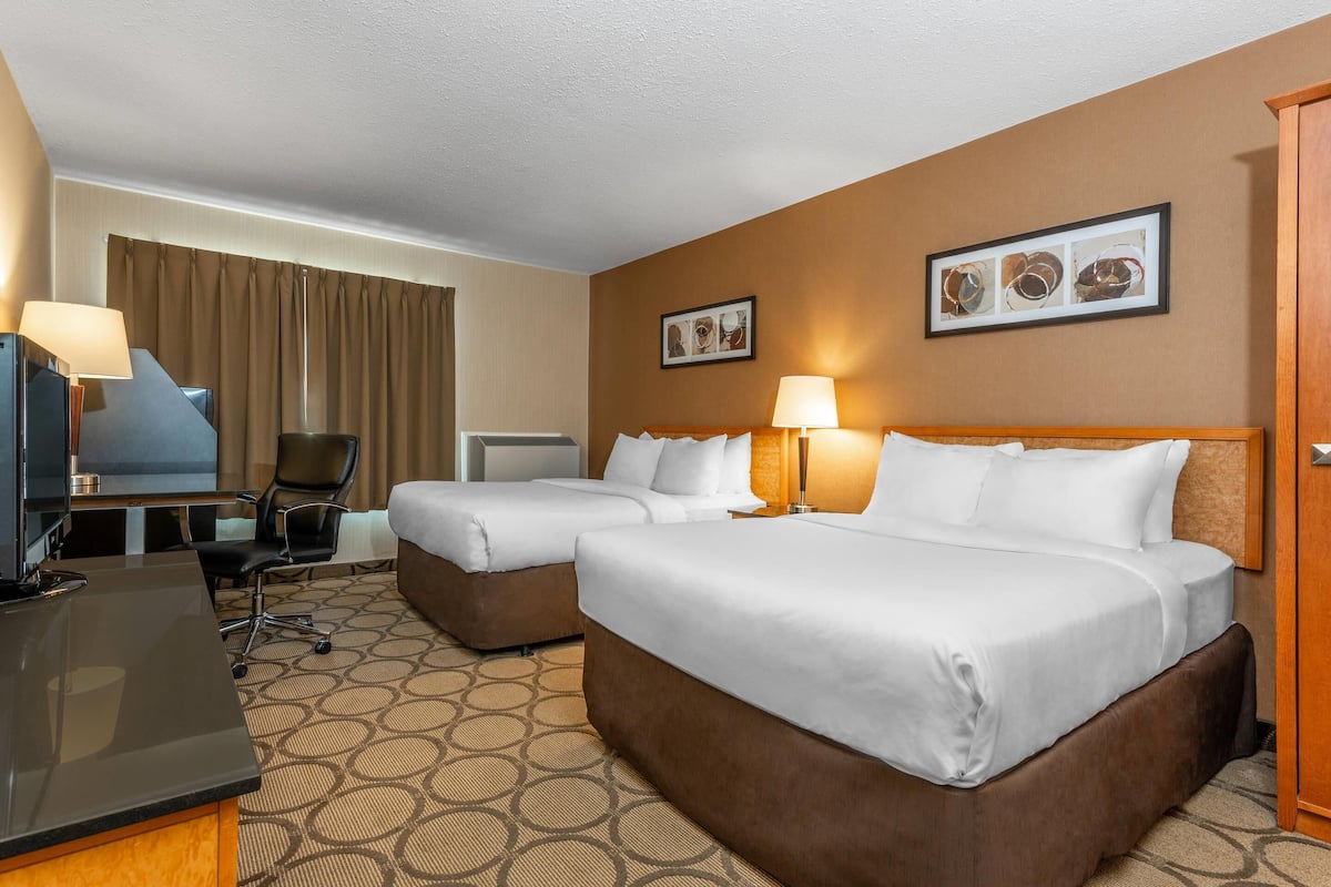 A hotel room with two beds, a desk, a chair, a television, and a door.