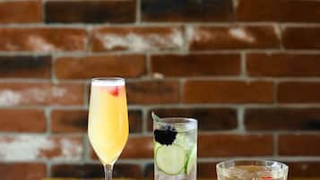 Three glasses of beverages on a wooden table against a brick wall.