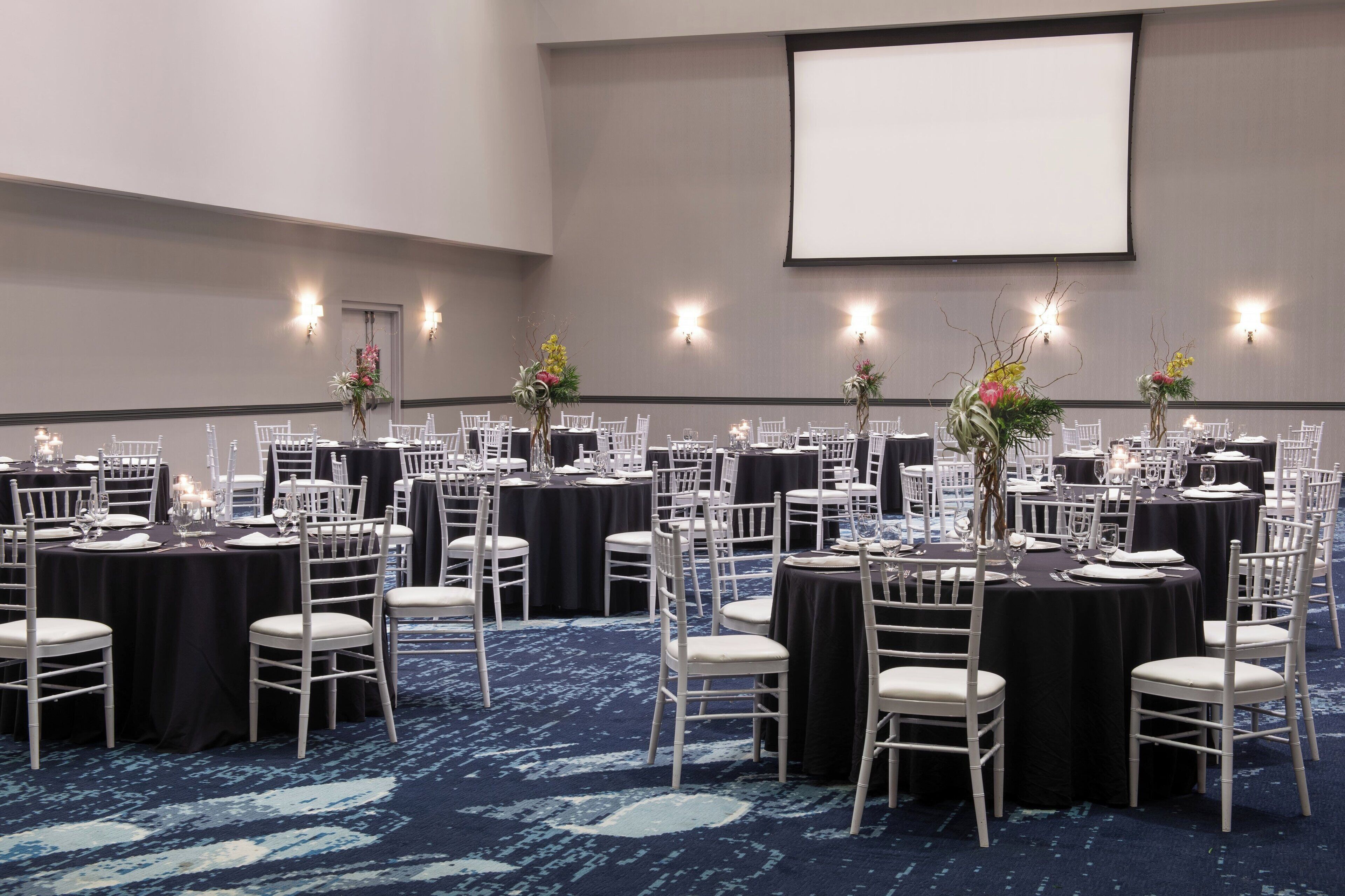 A conference room with round tables, white chairs, and floral centerpieces.