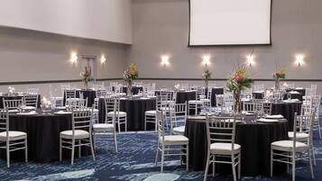 A conference room with round tables, white chairs, and floral centerpieces.