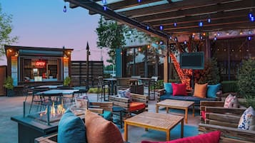 An outdoor patio area with wooden furniture, a fire pit, and string lights.