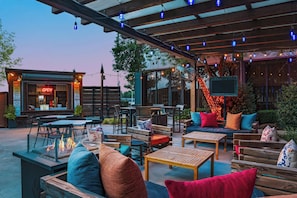 An outdoor patio area with wooden furniture, a fire pit, and string lights. - Sheraton Oklahoma City Downtown Hotel (Oklahoma City)